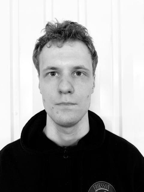 Black and white portrait photograph of a man with dark hair wearing a black hoodie against a white background